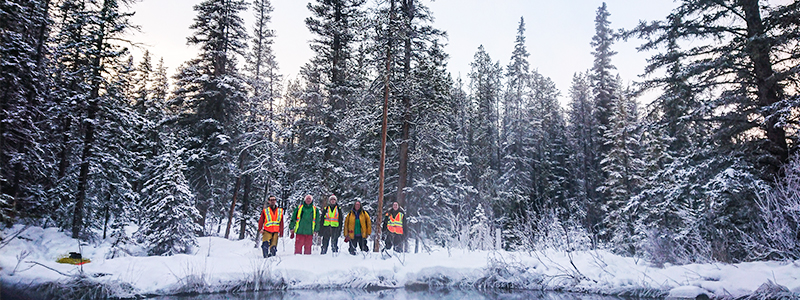 Alison Thompson and her team stand in front of a pond with a backdrop of spruce trees.